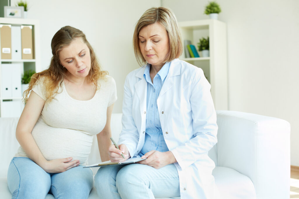 Young pregnant woman listening to prescription of doctor after regular examination at hospital